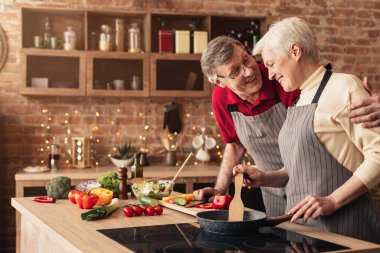 Happy Aged Couple Embracing And Cooking Dinner Together In Kitchen