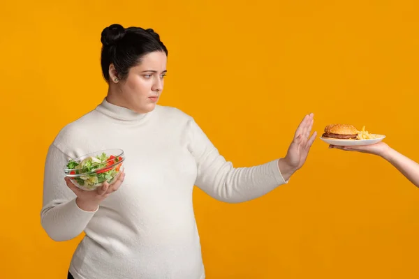 Ragazza in sovrappeso che rifiuta fast food, tenendo ciotola con insalata di verdure fresche — Foto Stock