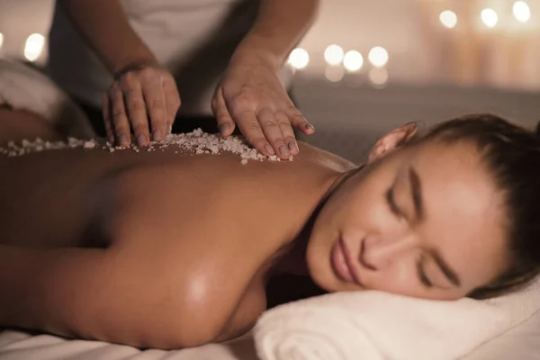 Beauty therapist pouring salt scrub on womans back — Stock Photo, Image