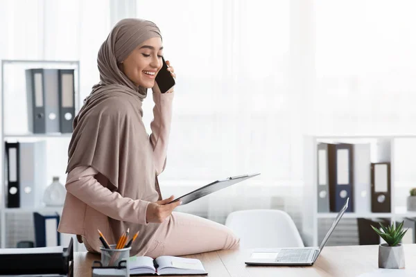 Modern arabic secretary talking on cellphone and holding clipboard in office — ストック写真