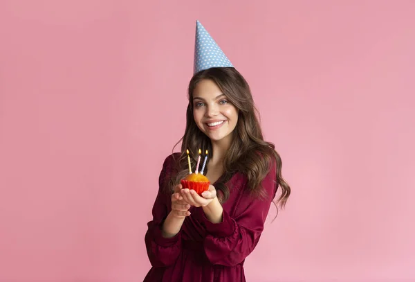 Happy girl in party hat holding birthday cupcake with lighted candles — Stok fotoğraf