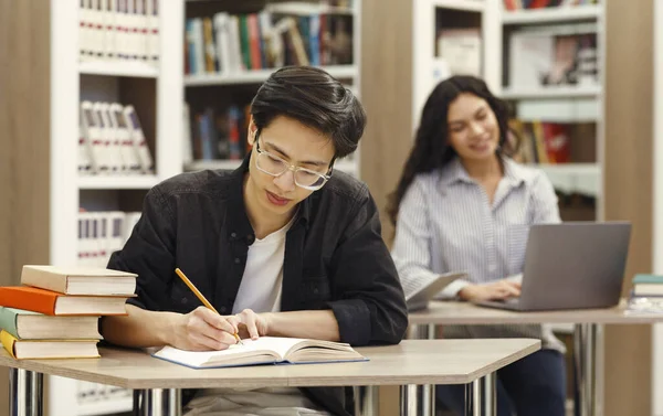 Asian guy doing research sitting at desk in library — Stockfoto
