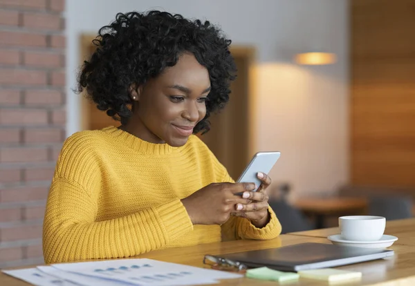 Busy cheerful black girl chatting at cafe, using smartphone — Stockfoto