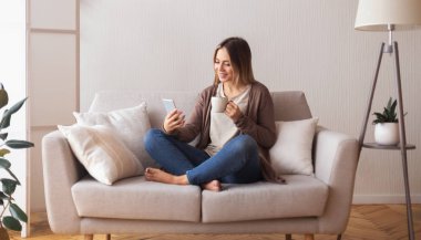 Cheerful woman with coffee talking with friends on cell phone