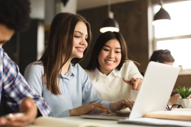 Diverse student girls networking on laptop in library