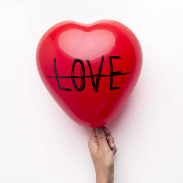 Female holding red heart balloon with crossed out love text — Stok fotoğraf