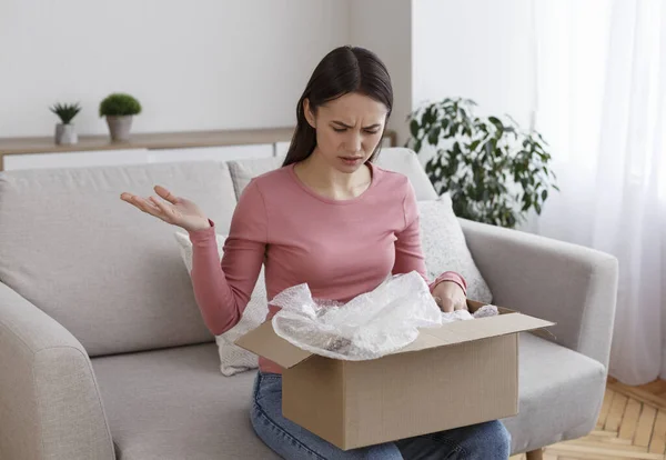 Dissatisfied young woman client open box from online internet shop