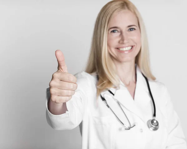 Happy middle-aged woman doctor in uniform with thumb up — Stockfoto