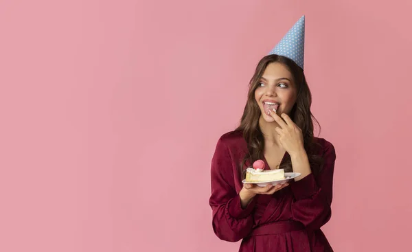 Pensive young girl in party hat eating cream of birthday cake — Stok fotoğraf