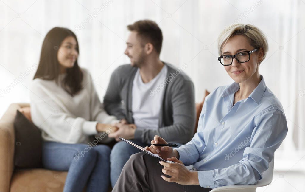 Family Psychologist Smiling While Couple Reconciling Sitting On Sofa Indoor