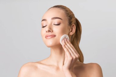 Attractive Girl Removing Makeup Using Cotton Pad Over Gray Background