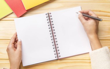 Female hands drawing in a spiral notebook at the wooden desk