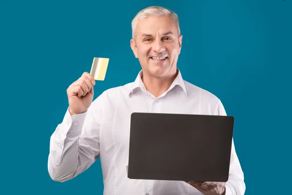 Happy mature man holding debit card and computer — Stock fotografie