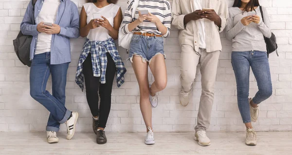 Cropped of multiethnic friends uisng smartphones, leaning on white wall — ストック写真