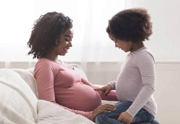 Curious little black girl touching her pregnant mothers belly at home — Stockfoto