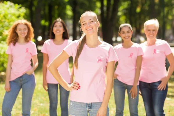 Chica con cinta de cáncer de mama de pie con voluntarios Grupo al aire libre —  Fotos de Stock