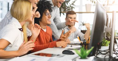 Happy young team celebrating professional success, looking at laptop screen
