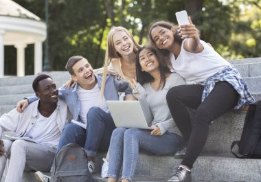 Happy multiethnic students taking selfie while studying in city