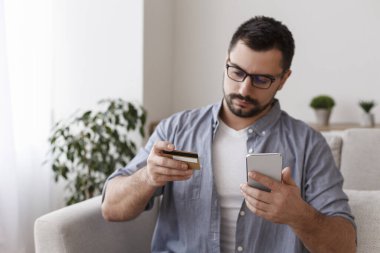 Young man with cellphone and credit card at home