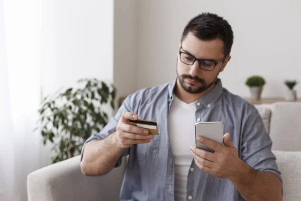 Young man with cellphone and credit card at home — Φωτογραφία Αρχείου