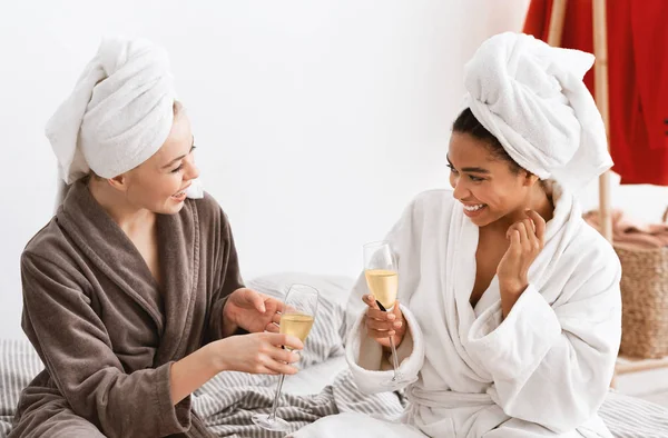 Multiracial girlfriends in bathrobes celebrating weekend, drinking champagne — Stockfoto