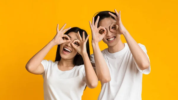 Cheerful asian couple in love holding fingers near eyes — Zdjęcie stockowe