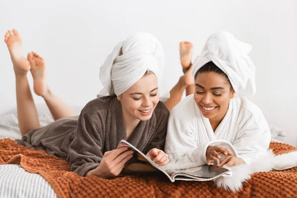 Carefree multiracial ladies reading magazine while having spa procedures — Zdjęcie stockowe