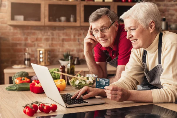 Happy senior couple using laptop and credit card in kitchen — ストック写真