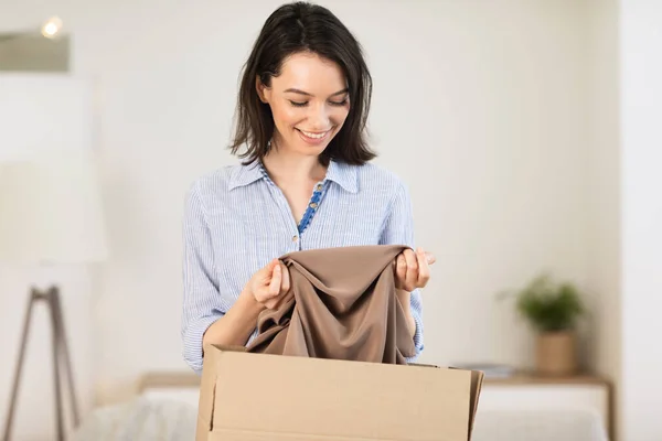 Happy young girl packing clothes in cardboard box