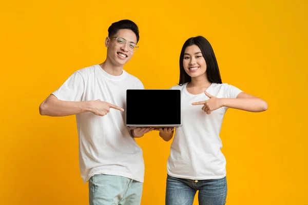 Young asian couple pointing at blank laptop screen — Stockfoto