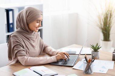 Ofisteki dizüstü bilgisayarda çalışan tesettürlü Arap iş kadını