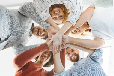 Millennial multiethnic team putting hands together, down low