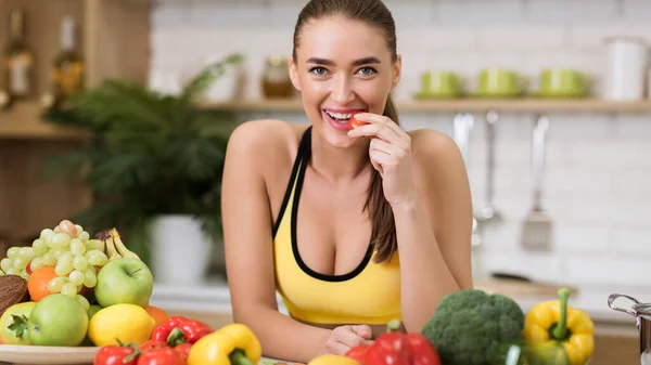 Mulher desportiva mordendo tomate cereja em casa cozinha — Fotografia de Stock