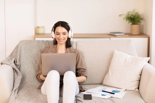 Fille écoute de la musique en ligne dans le casque assis sur le canapé — Photo