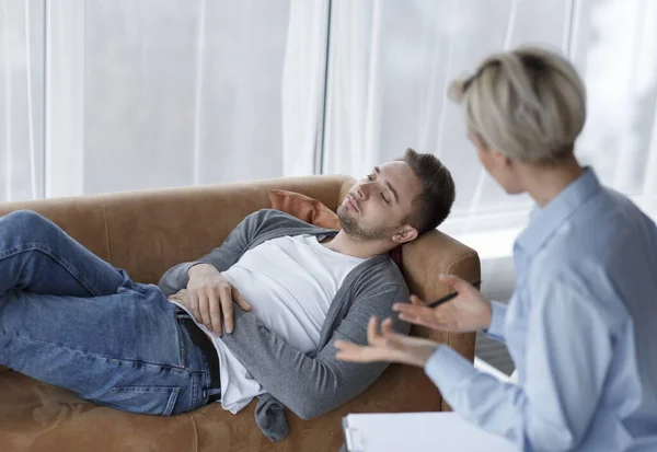 Paciente conversando com psicólogo deitado no sofá no escritório — Fotografia de Stock