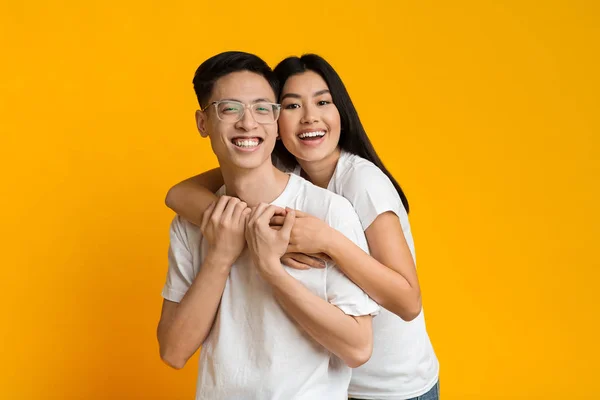 Emotional asian girl hugging her boyfriend over yellow background — Zdjęcie stockowe