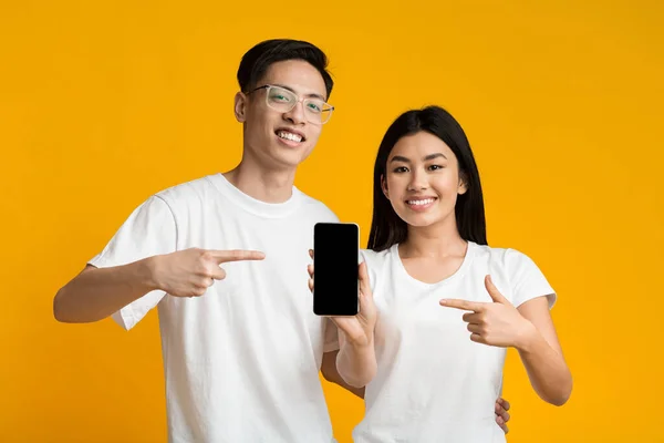 Cheerful asian couple showing smartphone with blank screen — Stok fotoğraf