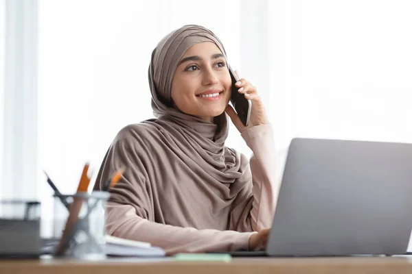 Arabic businesswoman talking on mobile phone while using laptop in office — Stok fotoğraf