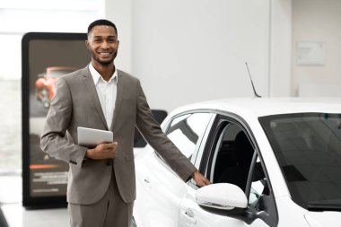 Salesman Selling And Showing New Car Standing In Luxury Dealership