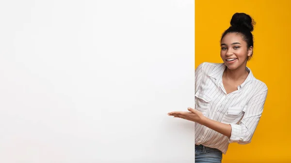 Smiling afro woman pointing at blank advertisement board with open hand — Stock Photo, Image
