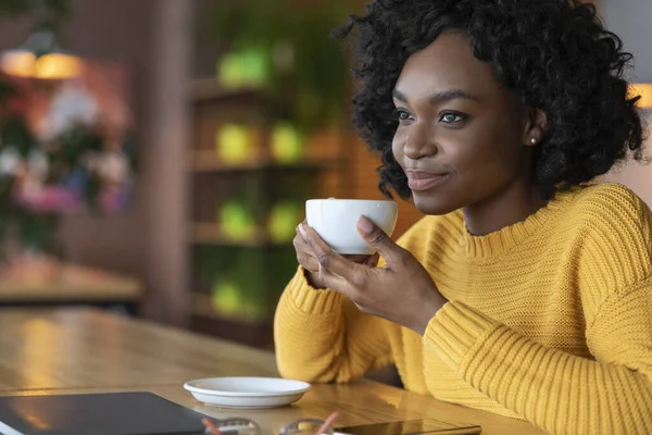 Jovem africana sonhadora relaxando no café, bebendo café — Fotografia de Stock