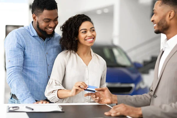 Spouses Giving Credit Card To Salesman Standing In Automobile Dealership — Stock Fotó