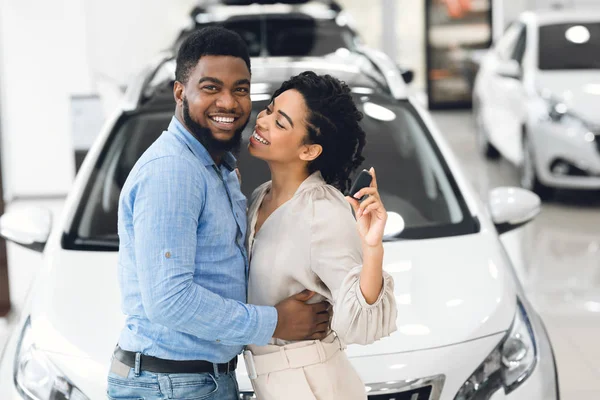 Casal mostrando novo carro chave abraçando em pé na loja de concessionárias — Fotografia de Stock