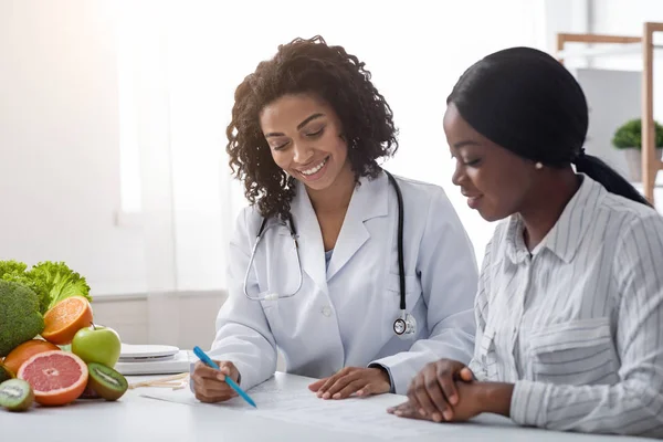 Donna africana nutrizionista che fa piano di trattamento per il paziente femminile — Foto Stock