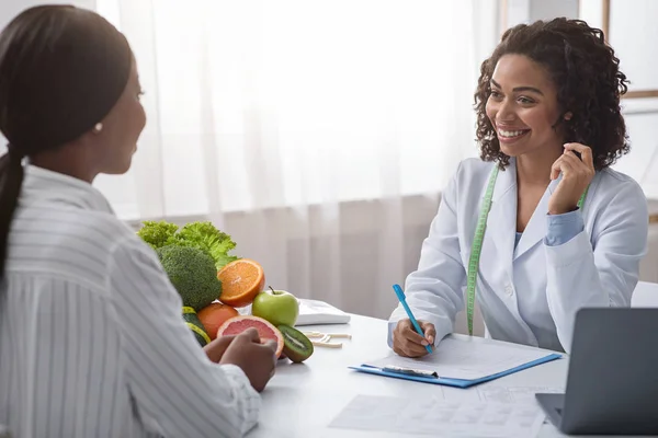 Smiling black woman talking to female patient, taking notes — Stok fotoğraf