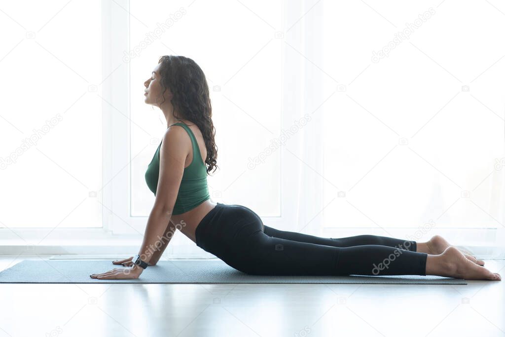 Attractive Latin woman doing yoga exercises at home. Cobra pose