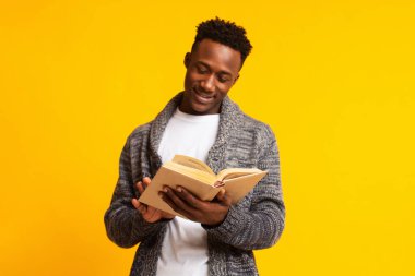 Handsome african guy reading interesting book over yellow