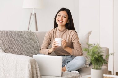 Enjoy weekend. Asian girl relaxing, drinking coffee and using laptop