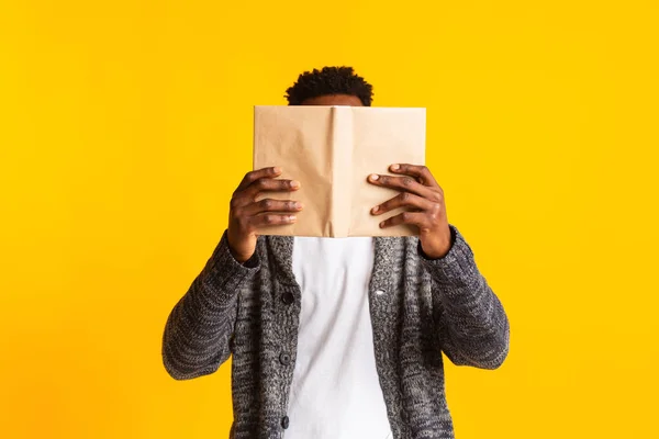 Africano americano em casaco de lã escondendo seu rosto sobre livro — Fotografia de Stock