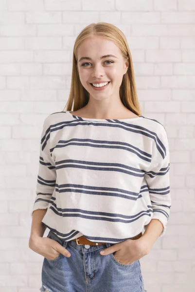 Pretty blonde girl with hands in pockets smiling over white — Stok fotoğraf
